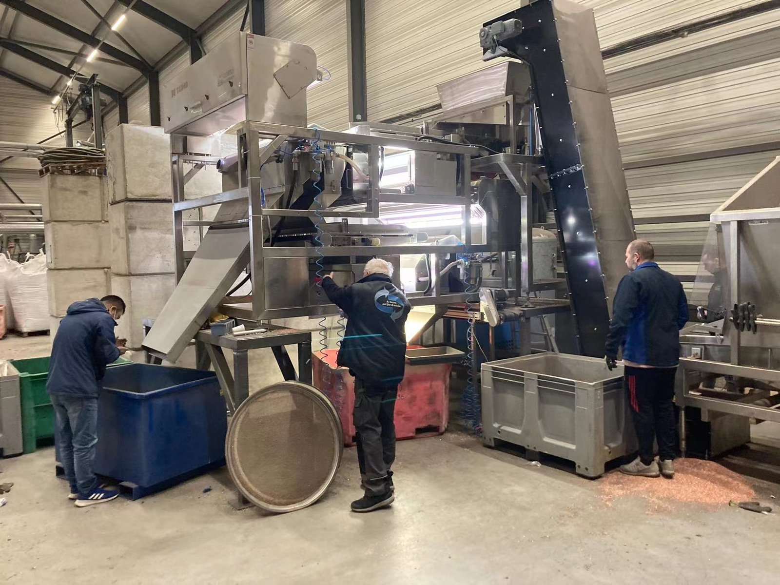 Two workers handling the optical sorting machine in a warehouse-looking building.